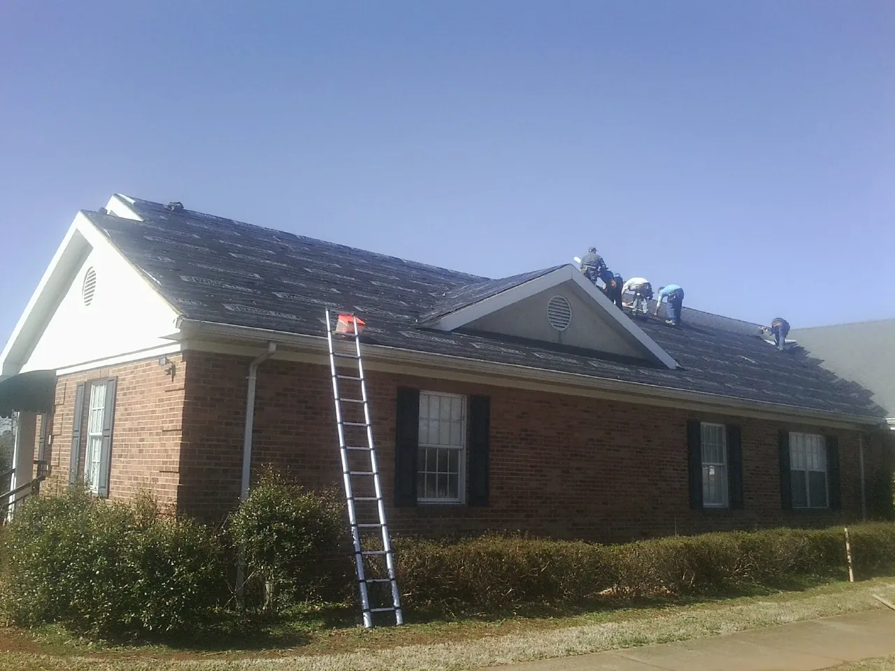 Crew tearing shingles off a brick ranch roof with a ladder set — Emergency Roof Repair work by our crew in La Crosse