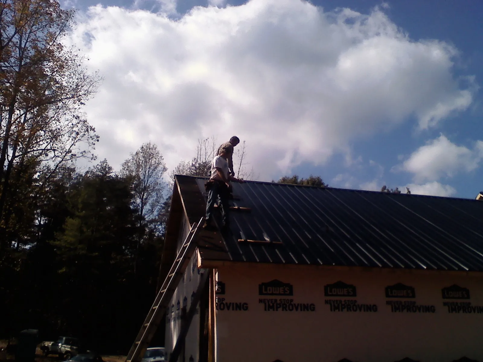 Roofer fastening dark metal panels high against a cloudy sky, from a Roof Inspection job in La Crosse